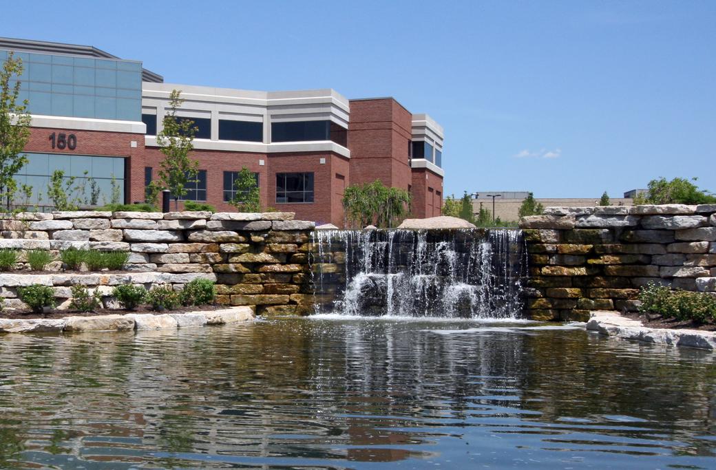 rocks, pond, and water fountain close by large building 