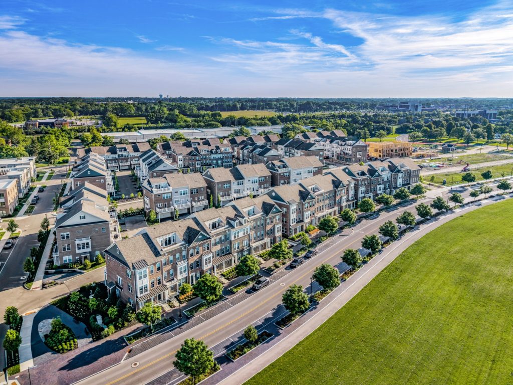 Rows of townhomes along John Shields Parkway are surrounded by street trees and paved walkways, with a traditional upscale architectural style.