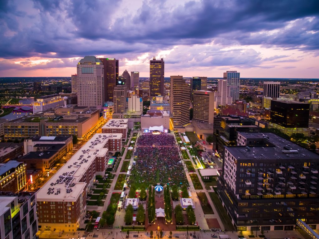 Nighttime view of Columbus Commons filled with people, a downtown public space and landscape architecture designed by EDGE.